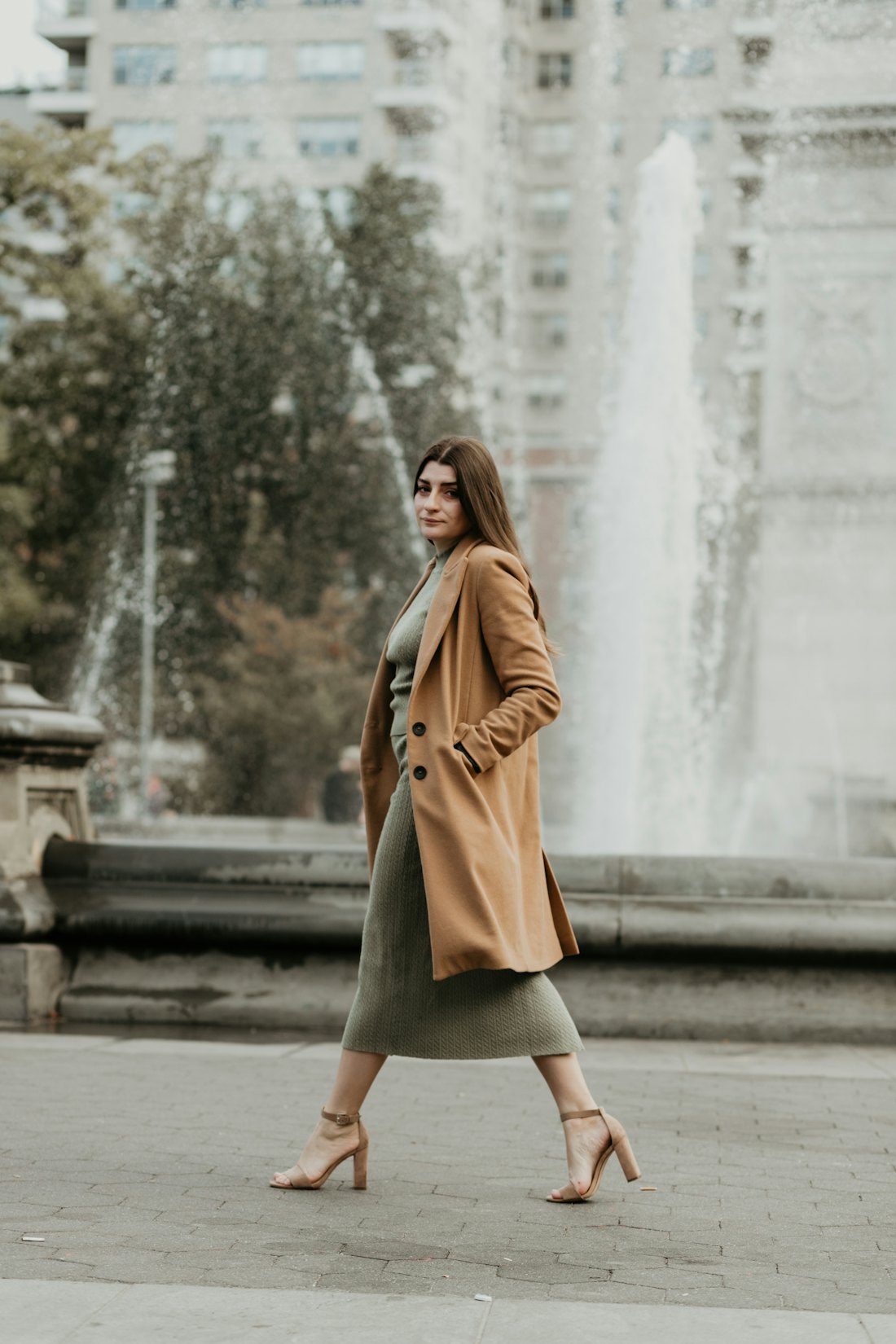 Frau im Trenchcoat vor einem Brunnen